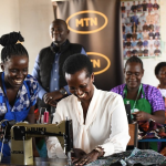 Allen Kagina, Trustee at MTN Foundation tries to saw clothes at Migeera Women Cente of Infleunce in Nakasongola District.