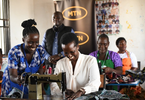 Allen Kagina, Trustee at MTN Foundation tries to saw clothes at Migeera Women Cente of Infleunce in Nakasongola District.